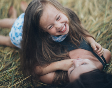 Bild zum Thema Gesundheitsmanagement zeigt eine Frau und ein Kind, die lachend im Getreidefeld liegen