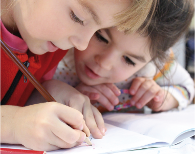 Bild zum Thema Lernoaching zeigt zwei Kinder, die gemeinsam in ein Heft schauen, während eines malt